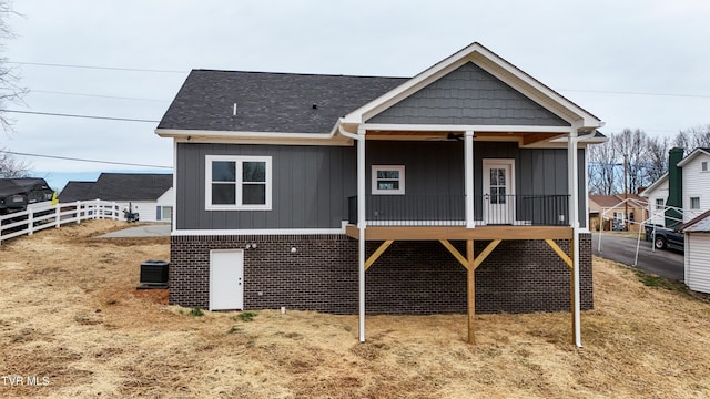 back of house featuring central AC, fence, board and batten siding, a shingled roof, and brick siding