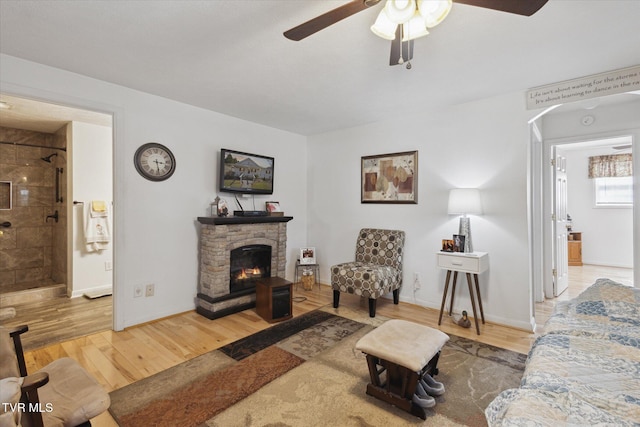 living room with baseboards, a fireplace, wood finished floors, arched walkways, and a ceiling fan