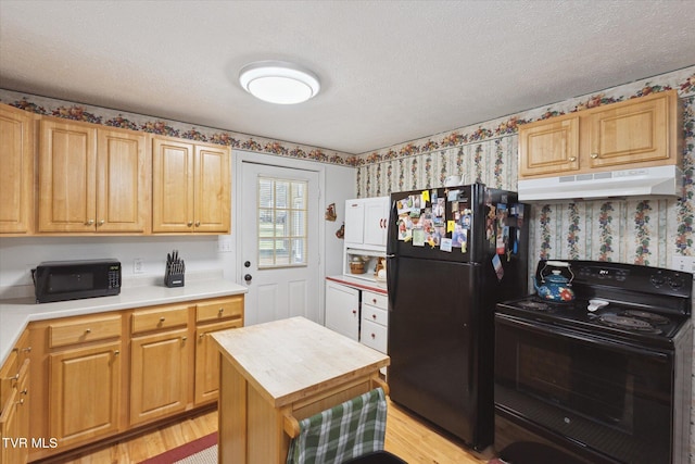 kitchen featuring light wood-type flooring, black appliances, under cabinet range hood, a textured ceiling, and wallpapered walls