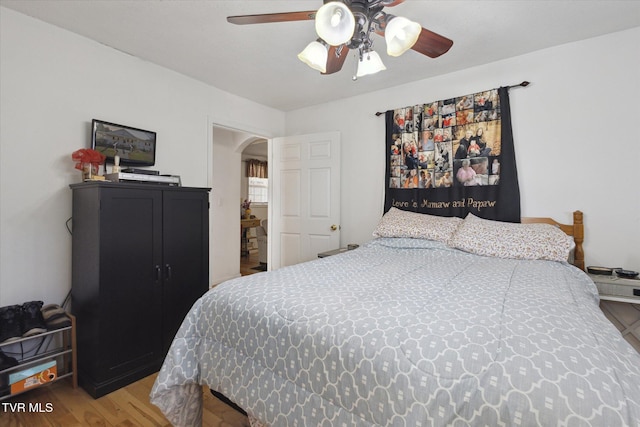 bedroom featuring arched walkways, wood finished floors, and a ceiling fan