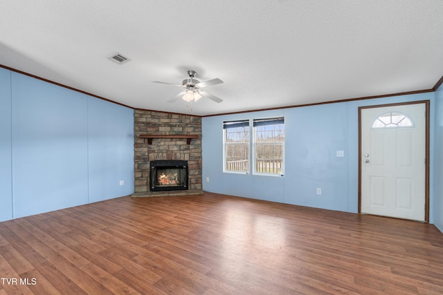 unfurnished living room with a stone fireplace, wood finished floors, visible vents, and crown molding