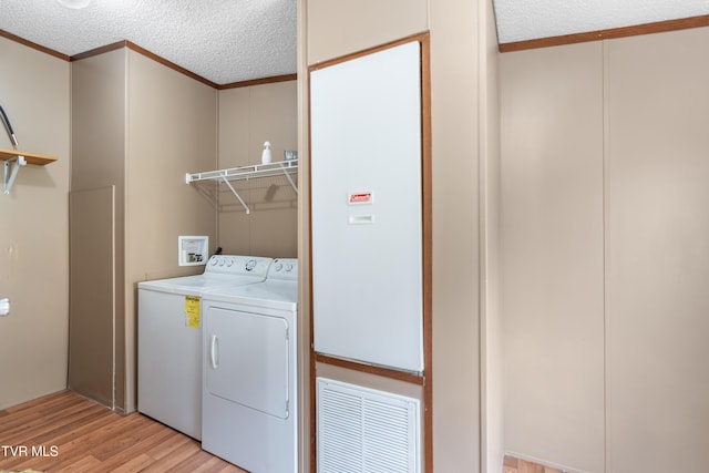 clothes washing area featuring crown molding, washer and clothes dryer, light wood-style flooring, a textured ceiling, and laundry area