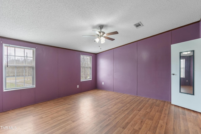 empty room featuring visible vents, ornamental molding, ceiling fan, a textured ceiling, and wood finished floors