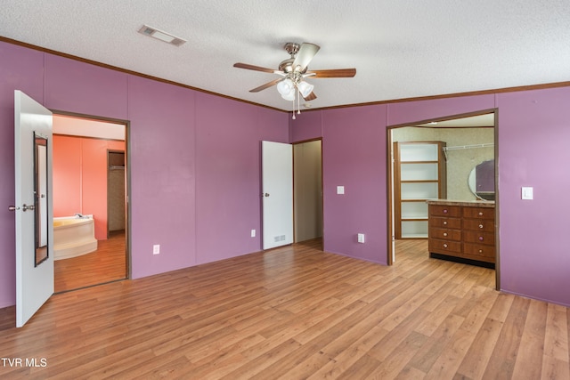 unfurnished bedroom with crown molding, visible vents, a spacious closet, a textured ceiling, and light wood-type flooring