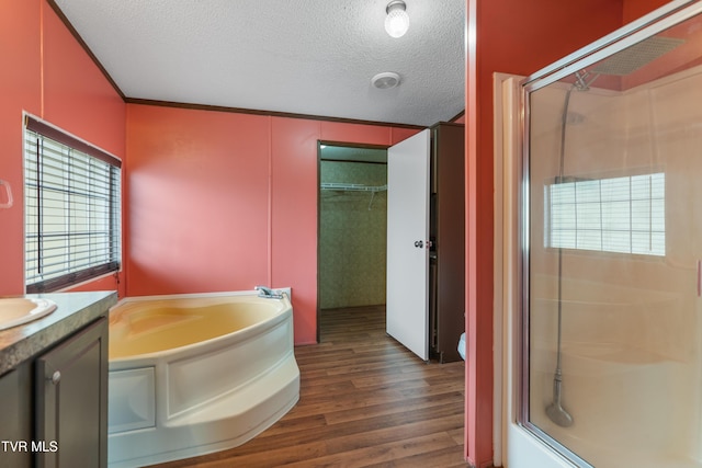 full bath featuring a textured ceiling, a garden tub, wood finished floors, vanity, and a stall shower