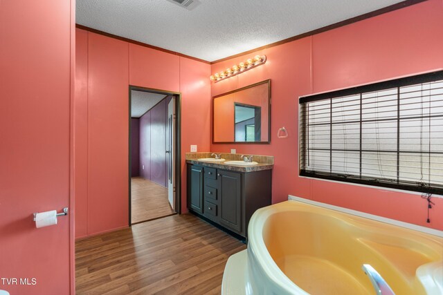 full bath with ornamental molding, a textured ceiling, vanity, wood finished floors, and a bath