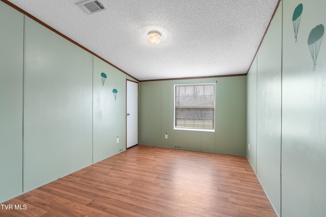 empty room with a textured ceiling, light wood finished floors, visible vents, and crown molding