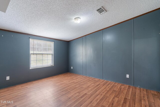 empty room with crown molding, a textured ceiling, visible vents, and wood finished floors