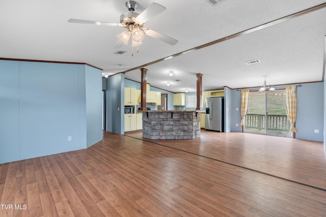 unfurnished living room with ceiling fan with notable chandelier, visible vents, vaulted ceiling, and wood finished floors