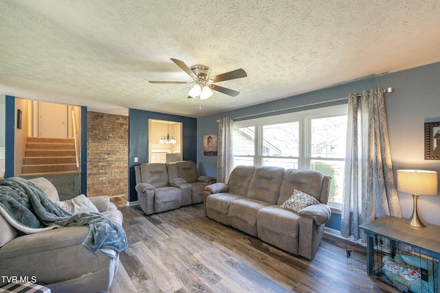 living room featuring a textured ceiling, stairway, wood finished floors, and ceiling fan with notable chandelier