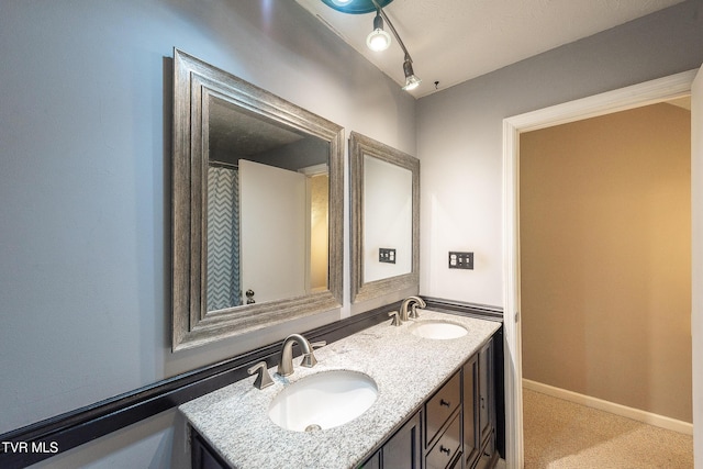 full bathroom with double vanity, a sink, rail lighting, and baseboards