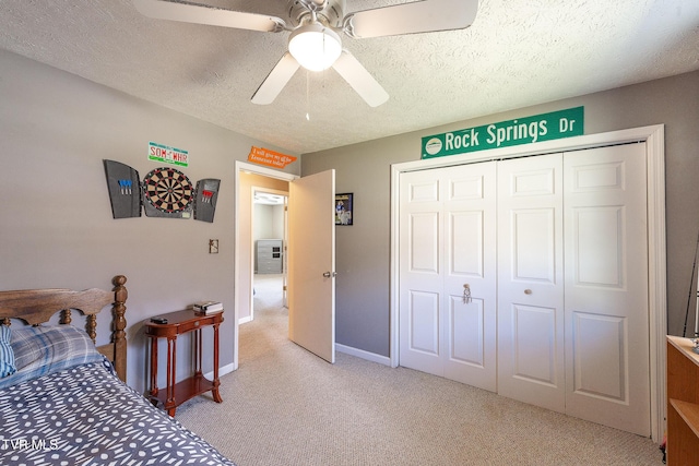 bedroom with a closet, light colored carpet, a ceiling fan, a textured ceiling, and baseboards