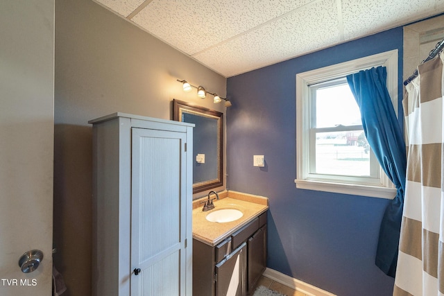 bathroom featuring a shower with shower curtain, a drop ceiling, vanity, and baseboards