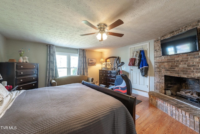 bedroom with ceiling fan, wood finished floors, a textured ceiling, a brick fireplace, and a closet