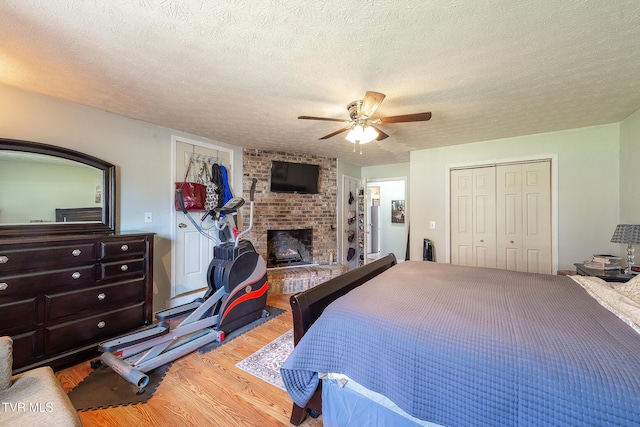 bedroom featuring a ceiling fan, wood finished floors, a textured ceiling, a brick fireplace, and a closet