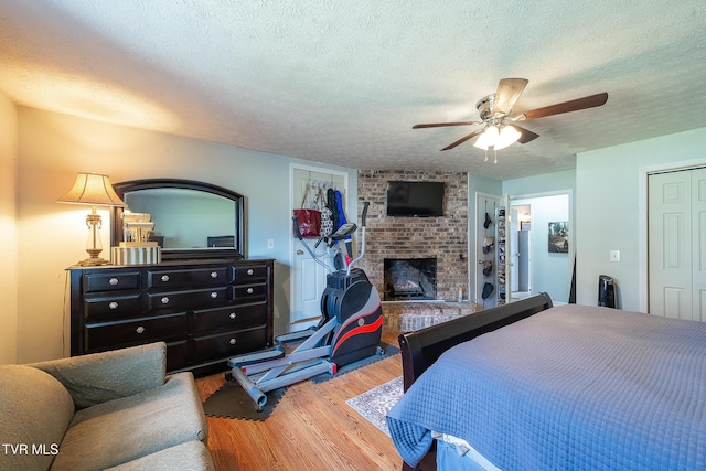 bedroom featuring a brick fireplace, a textured ceiling, a ceiling fan, and wood finished floors