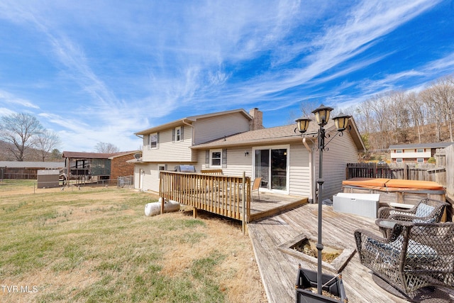 back of property with a hot tub, a chimney, a yard, fence, and a wooden deck