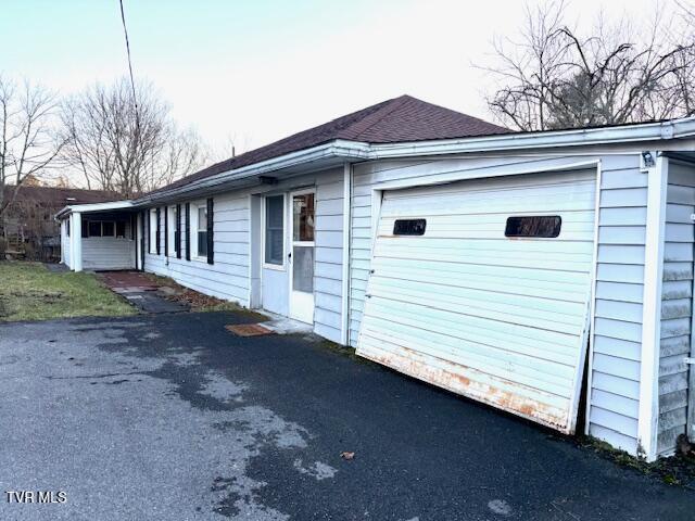 view of side of property featuring aphalt driveway, roof with shingles, and an attached garage