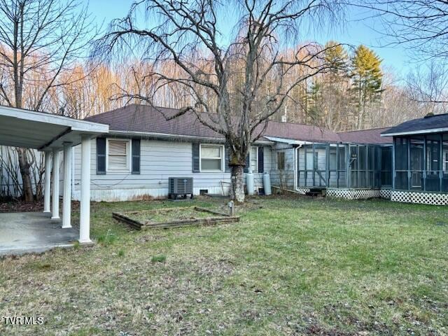 rear view of house with a carport, a sunroom, a lawn, and central AC unit