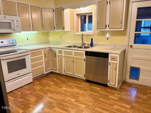 kitchen with light countertops, white appliances, light wood-type flooring, and a sink