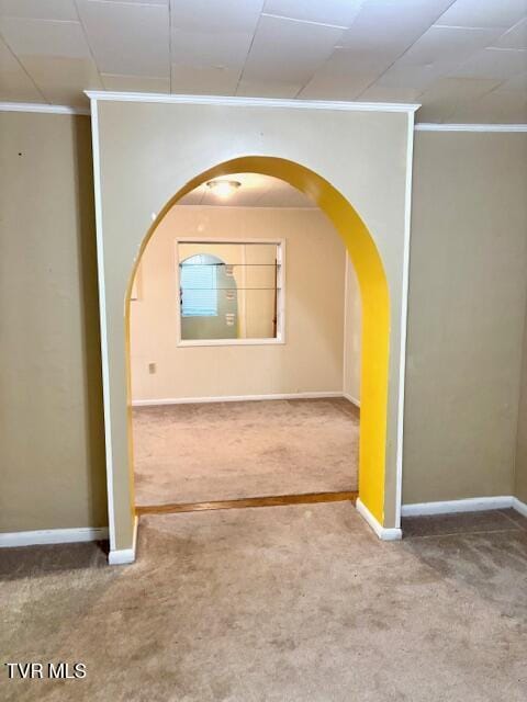 unfurnished room with arched walkways, carpet floors, ornamental molding, and baseboards