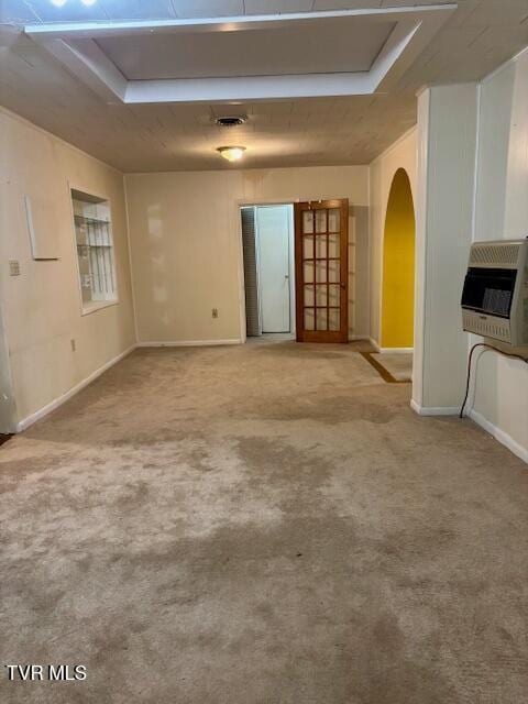 carpeted empty room with arched walkways, baseboards, visible vents, and heating unit