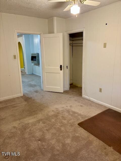 unfurnished bedroom featuring carpet, arched walkways, a closet, a ceiling fan, and a textured ceiling