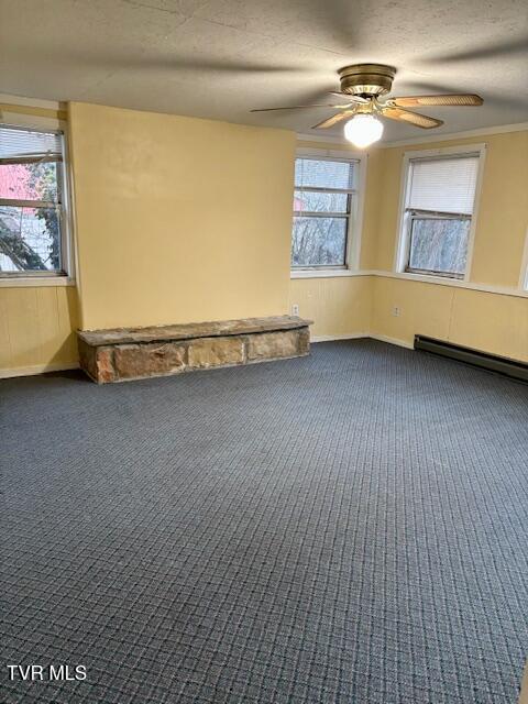 empty room with a baseboard radiator, a textured ceiling, dark colored carpet, and a ceiling fan