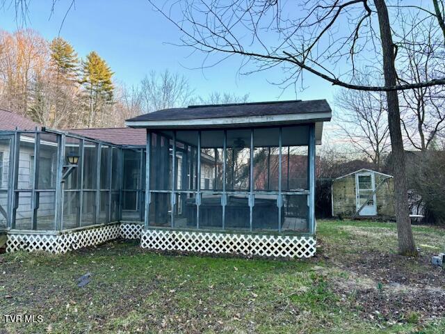 rear view of property with a sunroom, a shed, a lawn, and an outbuilding