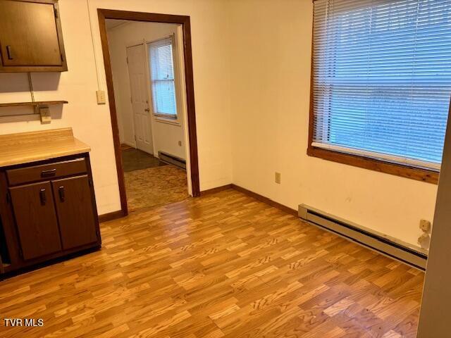 unfurnished dining area featuring light wood finished floors, baseboard heating, and baseboards