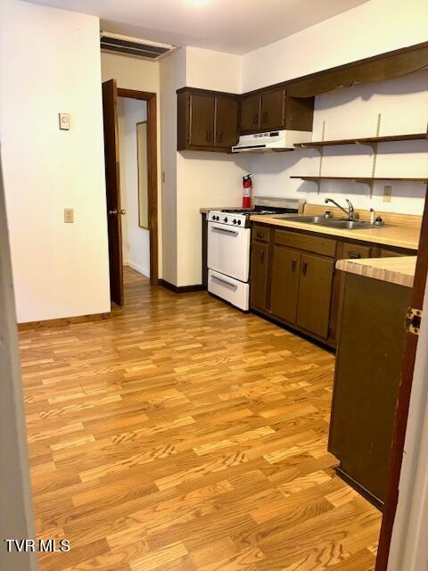 kitchen featuring under cabinet range hood, white range with gas cooktop, light wood finished floors, and a sink