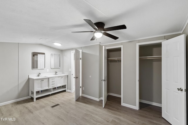 unfurnished bedroom featuring a sink, visible vents, multiple closets, and light wood-style flooring