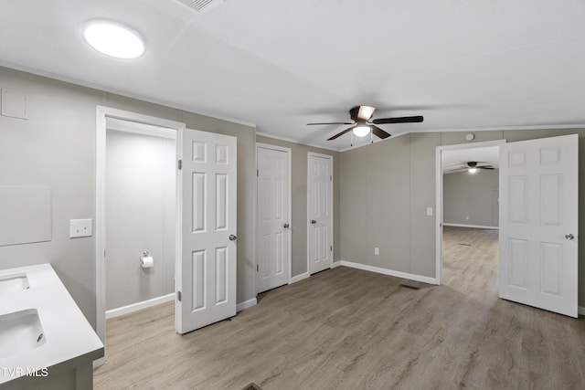 unfurnished bedroom featuring two closets, light wood-style floors, a ceiling fan, and a sink