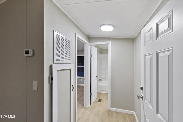 corridor with baseboards, visible vents, light wood finished floors, and a textured ceiling