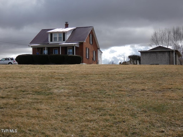 exterior space with brick siding, a chimney, metal roof, and a front yard