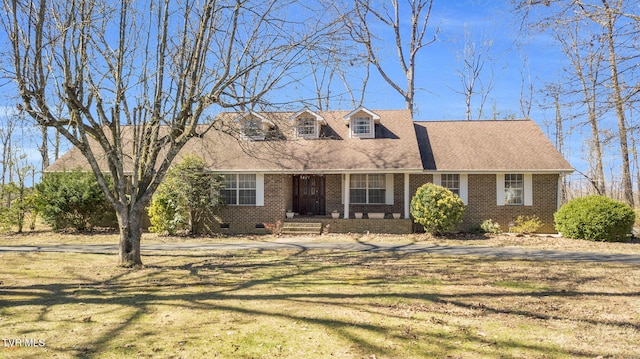 cape cod home with brick siding, crawl space, a front yard, and roof with shingles