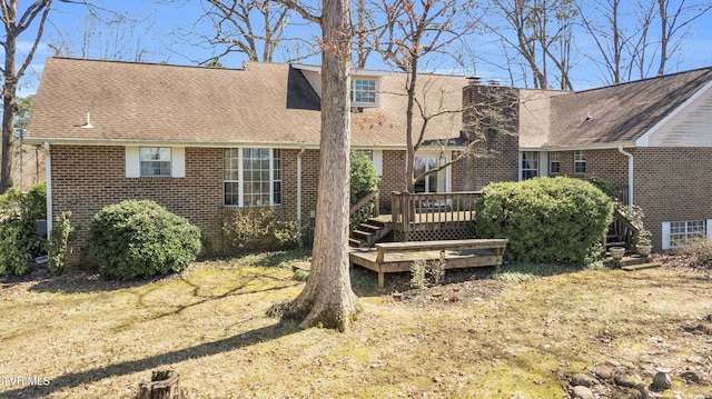 rear view of house featuring brick siding, a chimney, a deck, and roof with shingles