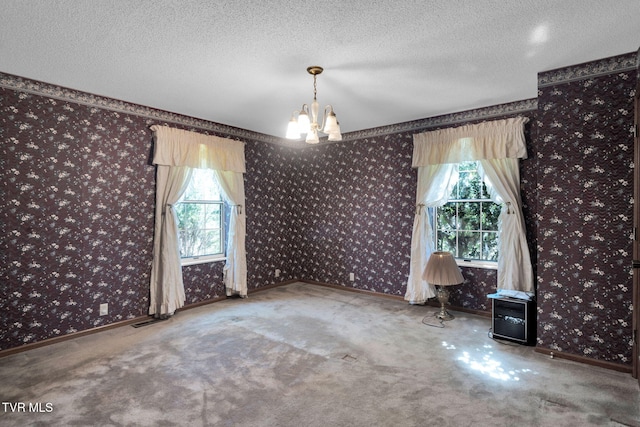 carpeted empty room with visible vents, a textured ceiling, wallpapered walls, baseboards, and a chandelier