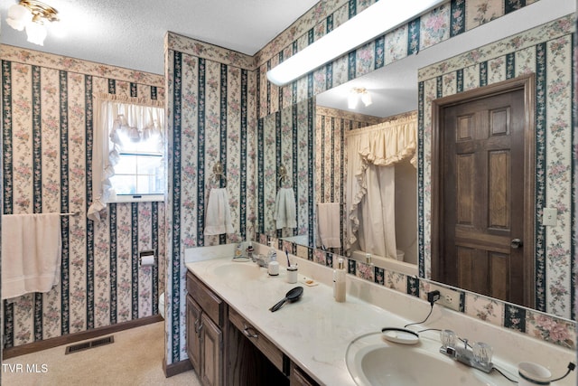 bathroom with a sink, visible vents, a textured ceiling, and wallpapered walls