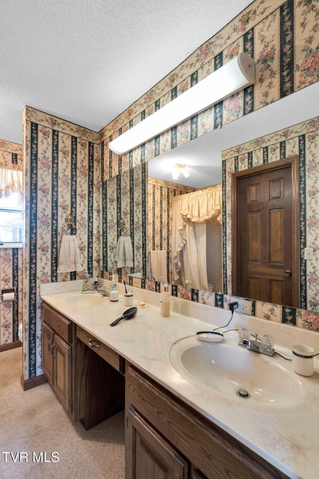 full bath featuring wallpapered walls, a textured ceiling, double vanity, and a sink