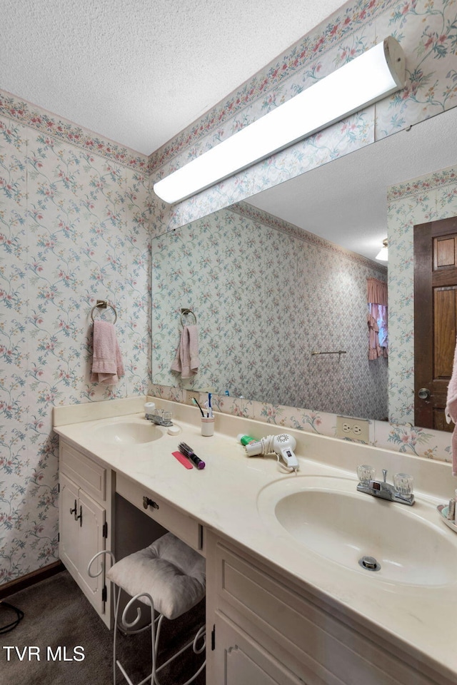 bathroom with a textured ceiling, wallpapered walls, and a sink