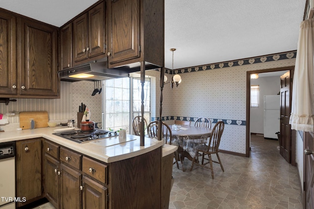 kitchen with wallpapered walls, under cabinet range hood, stainless steel electric stovetop, freestanding refrigerator, and stone finish floor