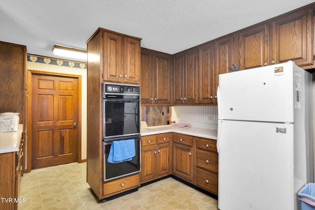 kitchen featuring brown cabinets, light countertops, dobule oven black, and freestanding refrigerator