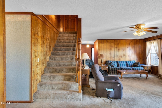 stairway with wooden walls, a textured ceiling, a ceiling fan, and carpet floors