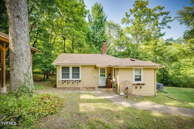 view of front of house featuring a front lawn, roof with shingles, central AC, and a chimney