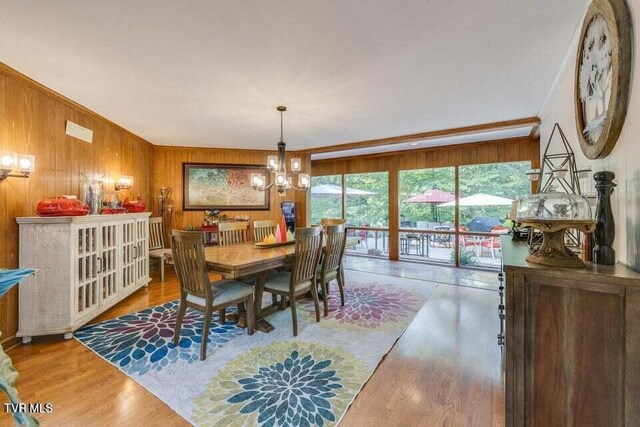 dining area featuring a notable chandelier, crown molding, wooden walls, and wood finished floors