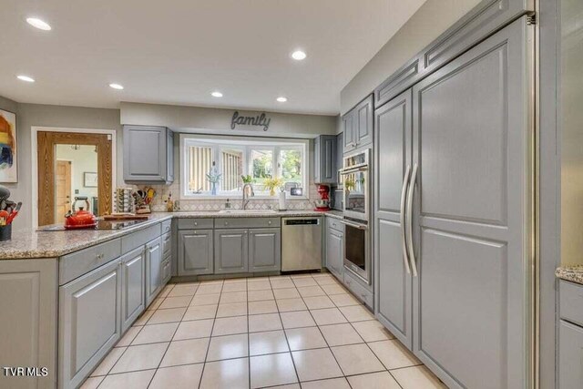 kitchen featuring gray cabinetry, light tile patterned floors, decorative backsplash, appliances with stainless steel finishes, and a sink