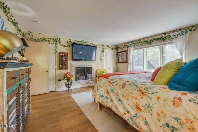 bedroom with a tiled fireplace, light wood-style flooring, and baseboards