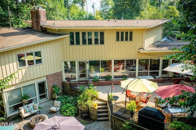 back of property with an outdoor living space with a fire pit, a patio area, brick siding, and a chimney