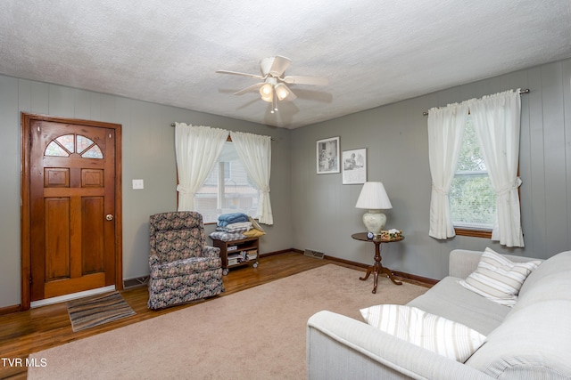 living area with baseboards, visible vents, ceiling fan, wood finished floors, and a textured ceiling